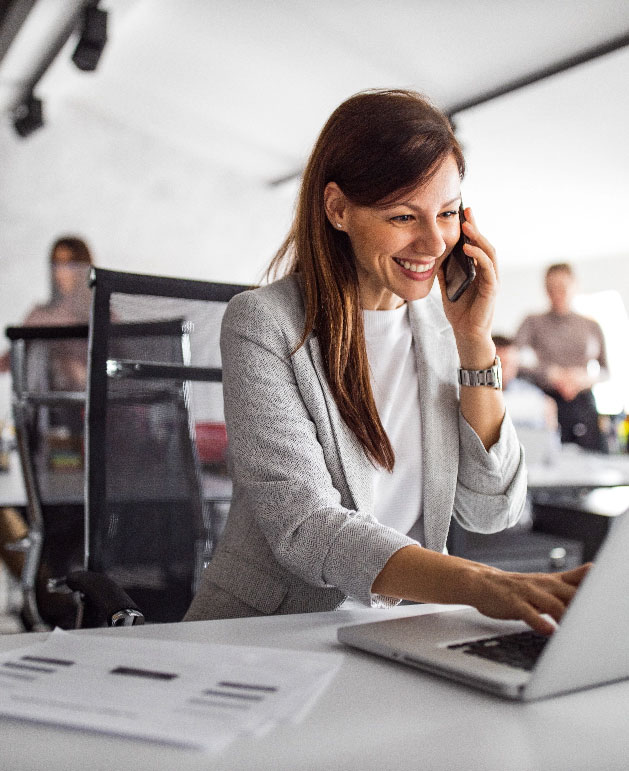 A person on the phone while working on a laptop at a desk