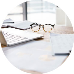 A desk with glasses, paper, and a laptop